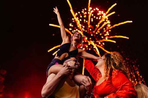 A group of joyful friends are partying at a concert on a summer night with stunning firework above them.