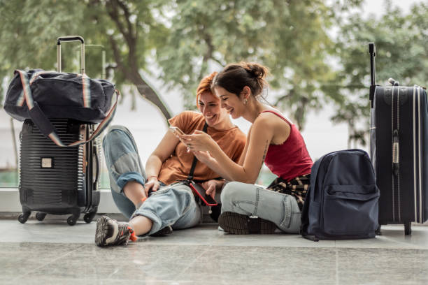 joven amiga usando el teléfono sentada en el suelo mientras espera en el aeropuerto - turismo argentina fotografías e imágenes de stock