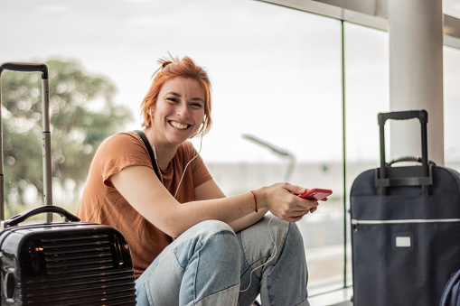 Portrait of a young woman using mobile phone sitting on ground at airport