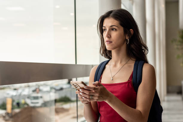 istock Young woman looking through while using mobile phone at airport 1492942545