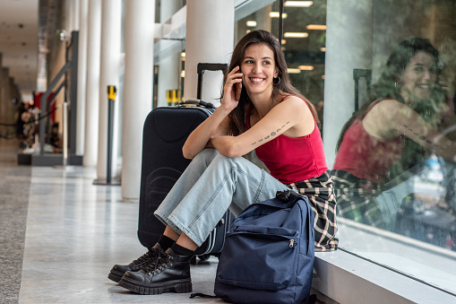 Young woman talking on mobile phone sitting on ground at airport