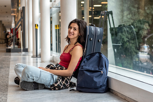 Portrait of young woman sitting on ground while waiting at airport