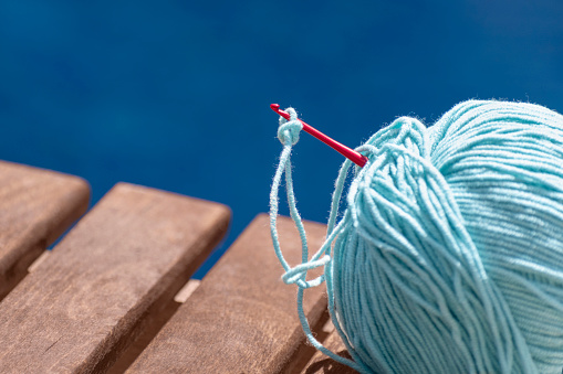 Ball of yarn for crochet on wooden bench isolated on blue swimming pool area background. Hobby, relaxation, needlework, knitting, handicraft, free time on summer vacation