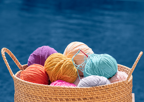 Knitting, crochet, needlework. Still life photo with multicolored wool skeins of yarn in basket isolated on blue background, close up. Hobby, relaxation, diy, handicraft during summer holidays