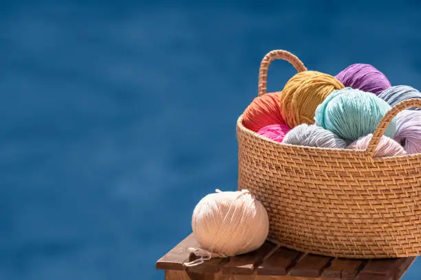 Knitting, crochet, needlework. Still life photo with multicolored skeins of yarn in basket isolated on blue background, copy space. Hobby, relaxation, creativity during summer holidays and recreation