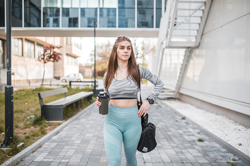 Female dancer dressed in sportswear is preparing for training, holding a sports bag and a reusable water bottle in her hands