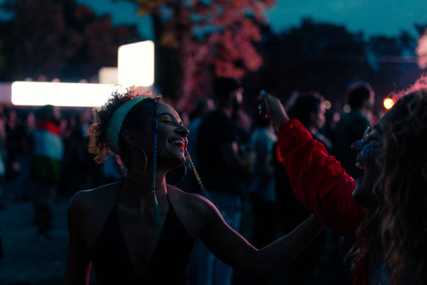 Two young adult girls are having a good time at concert on a summer evening, dancing in the dark.