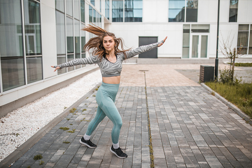 Beautiful young motivated woman dancer dressed in sportswear is training outdoors