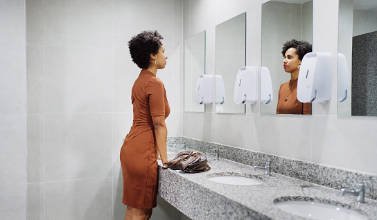 Young businesswoman standing in front of a mirror in an office bathroom and getting focused to do presentation