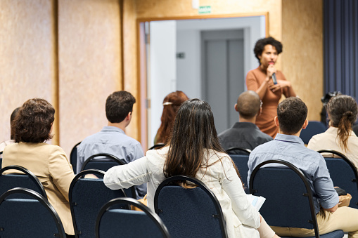 Rear view of a group of attendees listening to a speaker during a business seminar in a convention center