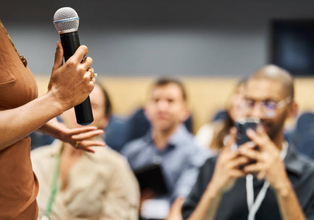 istock Businesswoman with a microphone speaking to attendees during a conference seminar 1492955126