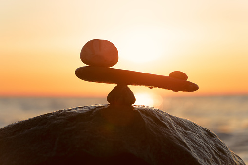 Imbalance of forces - natural scales of stones ( in imbalance) at the sea to the orange sunset - symbol photo