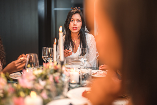 Beautiful Asian bride-to-be sitting at the elegantly set table, enjoying her bachelorette dinner with her close female friends.