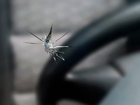 close up of a stone chip in the windshield of a car, detail shot of cracks in car glass on the drivers side.