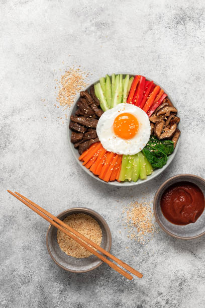 istock Korean Bibimbap. Rice with beef, vegetables, mushrooms and fried egg in a bowl. Top view, flat lay. Light grunge background. Vertical frame. 1492957668