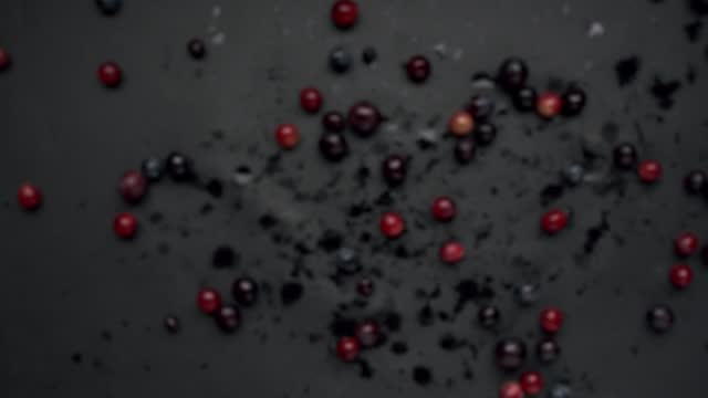 Fresh berries falling on wet surface in dark studio.