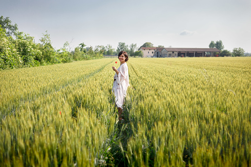 side view of smiling woman in white dress walking in grain field
