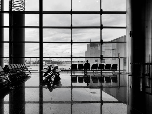 A person sitting in the boarding area, just the silhouette of the person, and in the background, behind the glass, the runway and planes.
