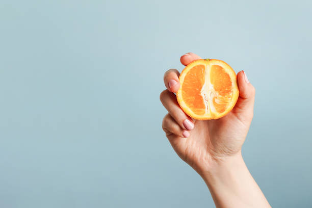istock Female hand holding orange on blue background, copy space 1492963338