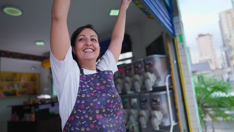 Female Business Owner of Local Store opening garage storefront. Young entrepreneur woman wearing apron starting the day routine