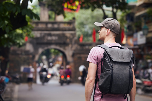 Traveler walking on busy asian street. Rear view of man with backpack in Old Quarter in Hanoi, Vietnam.