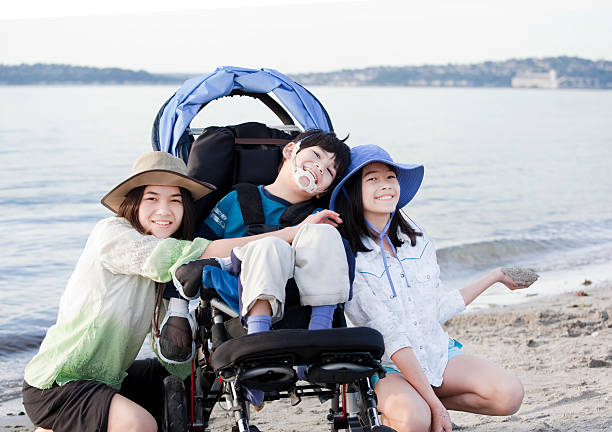 Sorelle che si prende cura di disabili fratello sulla spiaggia - foto stock