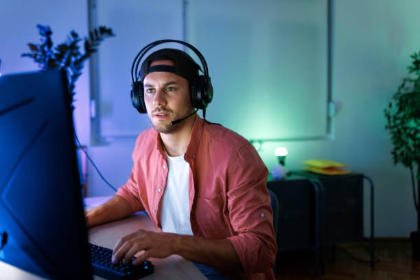 Young handsome man with hat and headset playing video games on desktop PC at home