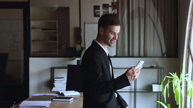 Smiling millennial business man using smartphone at workplace