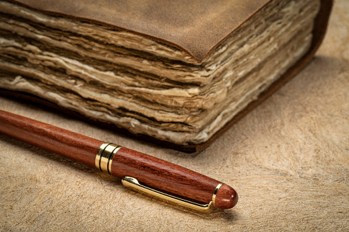 stylish wooden pen and a retro leather-bound journal with decked edge handmade paper pages on a textured bark paper, journaling concept