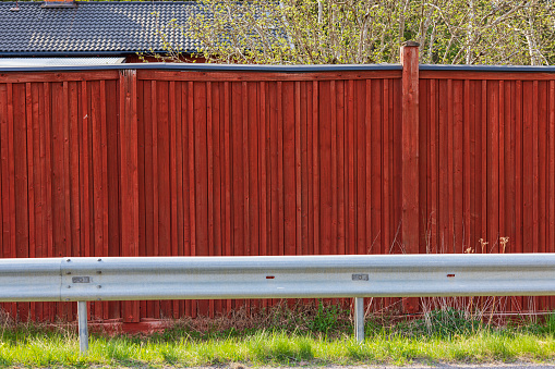 View of red wooden fence and tile roof of residential building behind. Sweden.