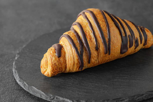 istock Croissant with chocolate stripes, on slate stone plate round, dark background, side view, selective focus 1492981082