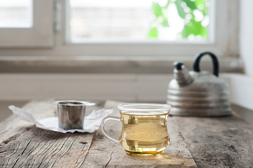 Freshly made white tea on a weathered wooden board with vintage teapot in the background