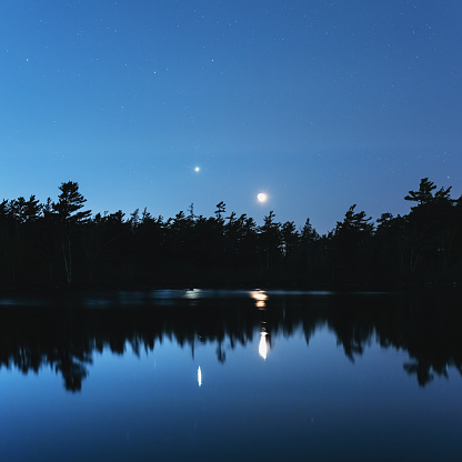 Venus shines with the crescent Moon above a still lake. Long exposure.
