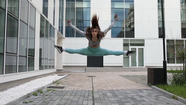 A young female dancer dressed in sportswear practices jumping with completely straight legs