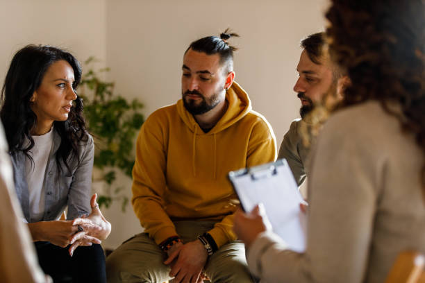 Anxious young woman sharing her struggles with her peers during a group therapy session stock photo