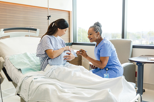 The mid adult mother shows the senior adult female doctor her new baby.