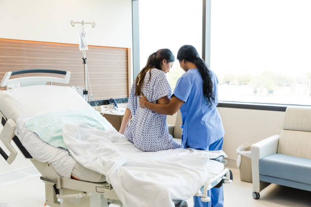 Unrecognizable female nurse helps woman get out of hospital bed stock photo