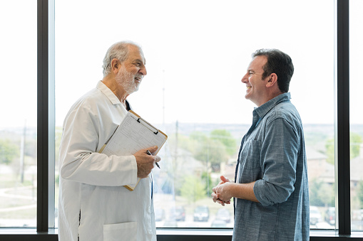 The mid adult man smiles with relief while talking to the senior adult male doctor.