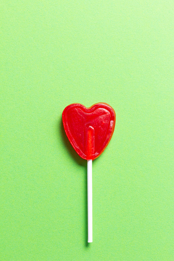 Heart shaped candy lollipop in red on a green background.