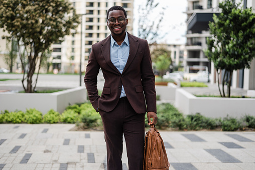 Handsome black businessman confidently standing on city street and smiling while looking at camera.
