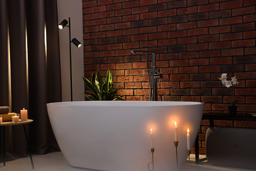 Stylish bathroom interior with ceramic tub and burning candles