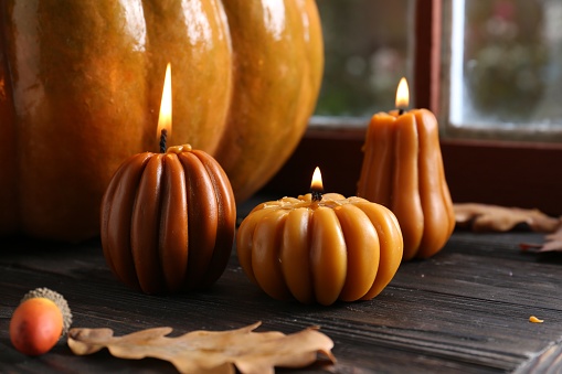 Beautiful burning candles in shape of pumpkins on wooden table near window. Autumn atmosphere