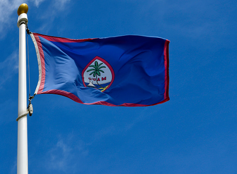 Hagåtña, Guam: flag of Guam fluttering in the wind - the flag of the United States territory of Guam was adopted in. The territorial flag is dark blue with a red border on all sides. The red border represents the blood spilled in World War II and Spanish sovereignty. In the center of the flag is the seal; an almond-shaped emblem, which depicts a proa boat sailing in Hagåtña Bay, and 'GUAM' in red letters. The landform under the coconut palm tree depicts the Two Lovers Point in Guam.