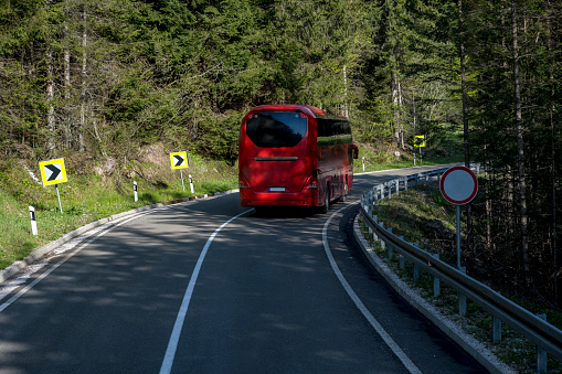 Red bus on a mountain road. Travel through the mountainous regions of the desert. tourist trip. back view. Touristic Red bus on highway. Red bus in the road of Serbia and green forest at sides.