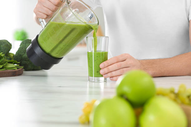 istock Man pouring delicious smoothie into glass at white marble table, closeup 1493008496