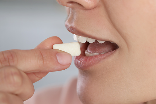 Woman putting chewing gum into mouth on blurred background, closeup