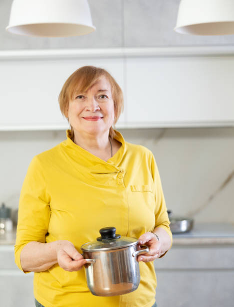 mulher adulta posando com panela na cozinha - home interior women domestic kitchen cabinet - fotografias e filmes do acervo