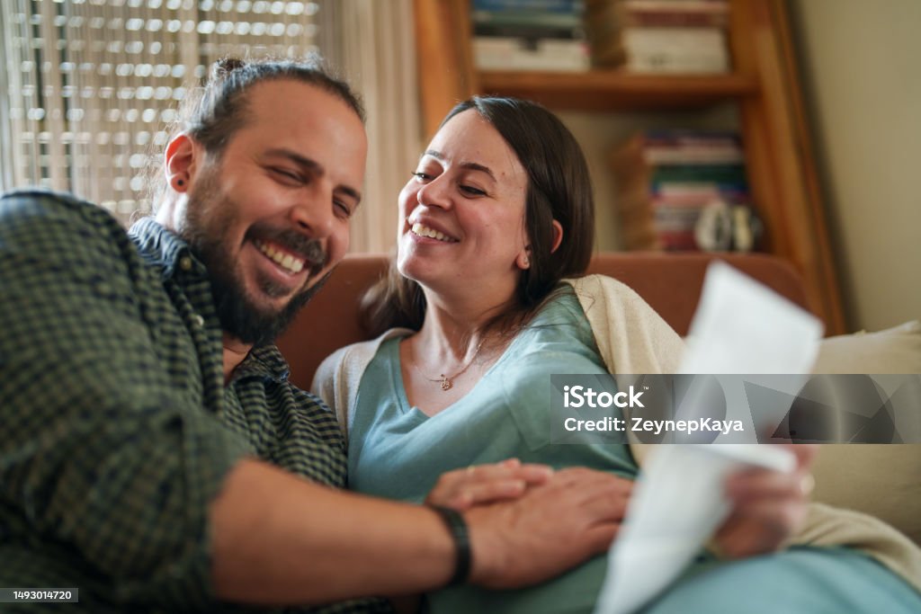 Expectant Couple looking ultrasound images of baby in living room Expectant Family in living room Couple - Relationship Stock Photo