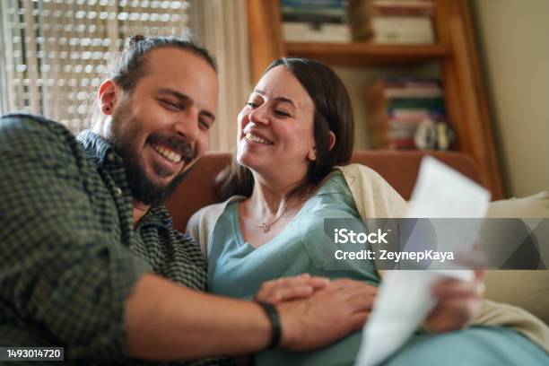 Expectant Couple Looking Ultrasound Images Of Baby In Living Room Stock Photo - Download Image Now