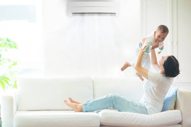 Mother and child with air conditioner remote Asian mother and child with air conditioner remote control. Comfortable temperature at family home. Cooling device. Mom and baby boy on couch under cold breeze. Air conditioning on hot summer day. air conditioner family stock pictures, royalty-free photos & images